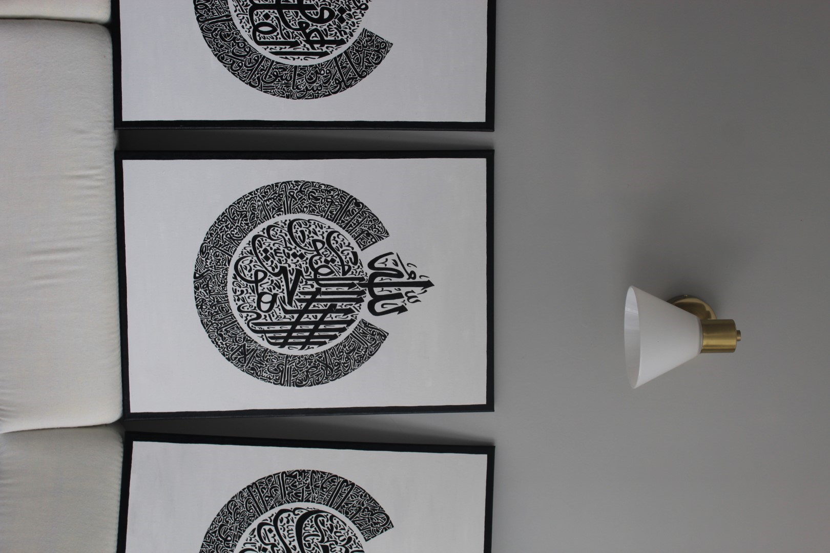Arabic calligraphy artworks by Tugram.art, displayed in black frames on a grey wall